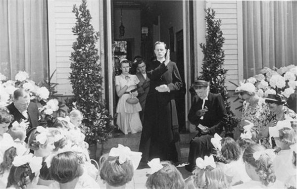 H.M.M. Schröder (1927-1993) zegent op de dag dat hij zijn eerste mis heeft opgedragen, voor de deur van zijn ouderlijk huis, zijn knielende ouders en een groep bruidjes die hem van de kerk naar zijn ouderlijk huis hebben vergezeld. Tilburg 1952